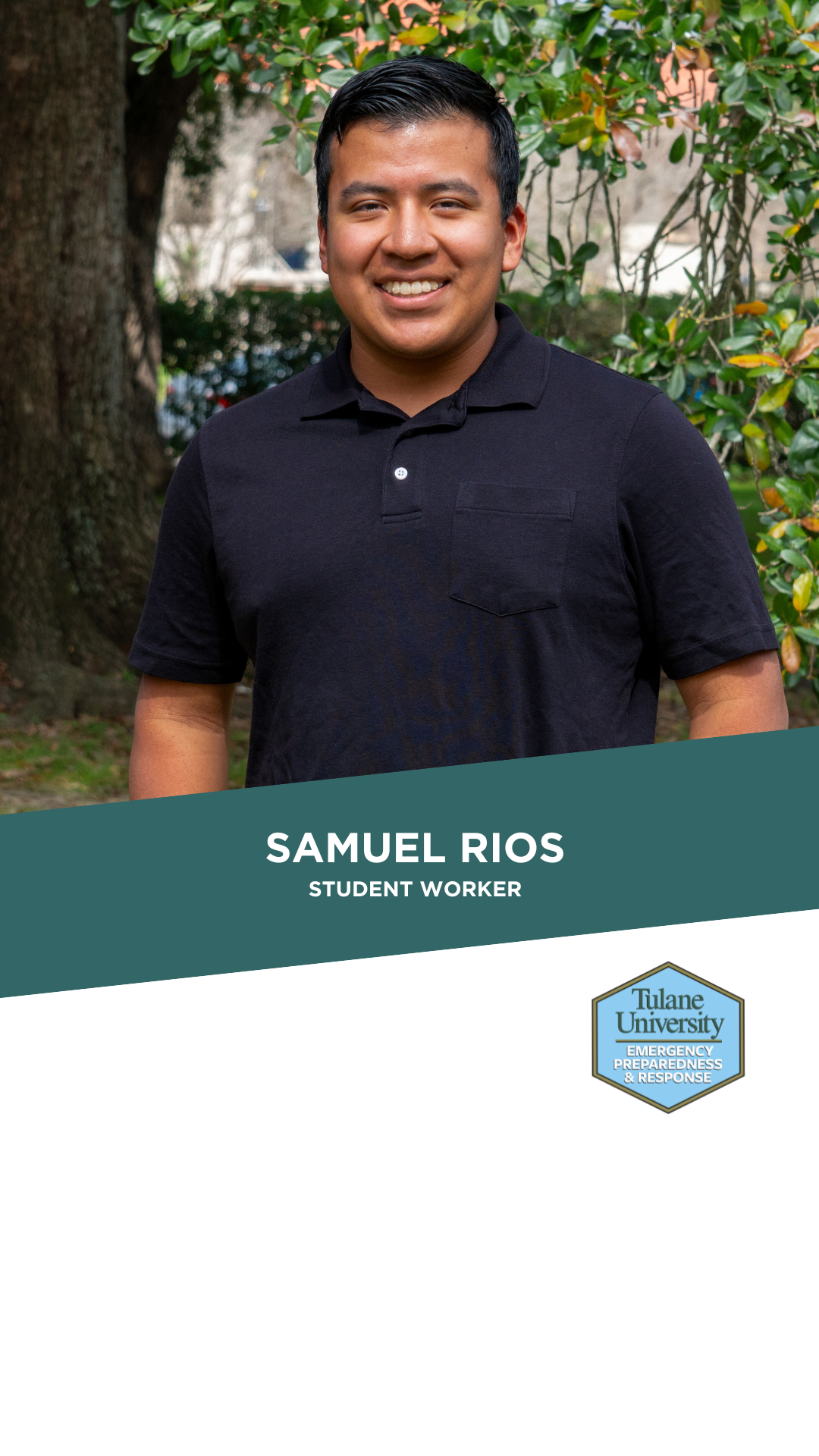 Smiling man in a dark polo shirt standing outdoors with green trees.